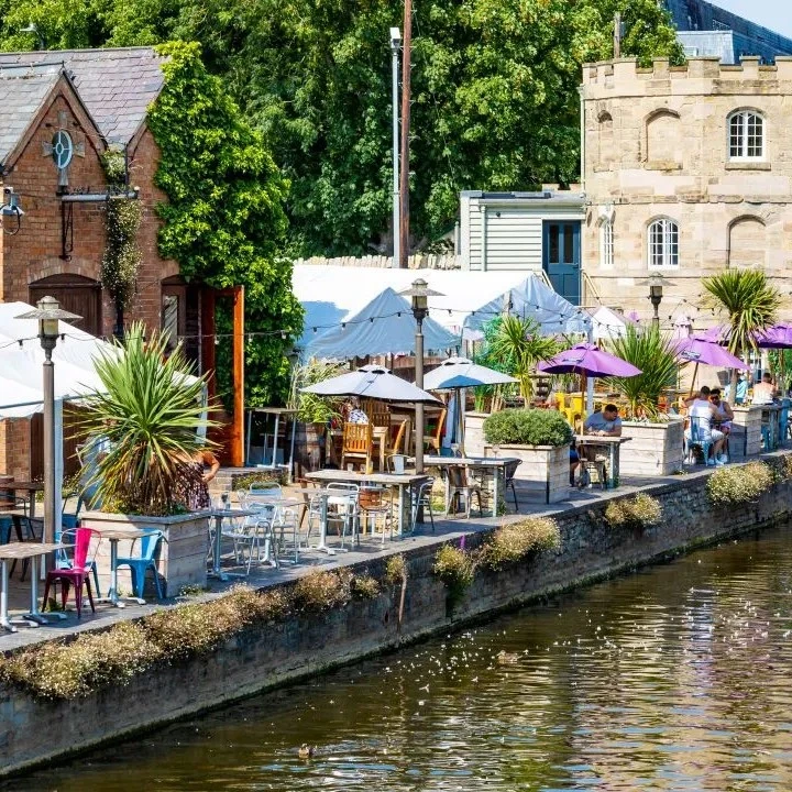 A row of restaurant tables by the river with people sitting and eating in Stratford-upon-Avon